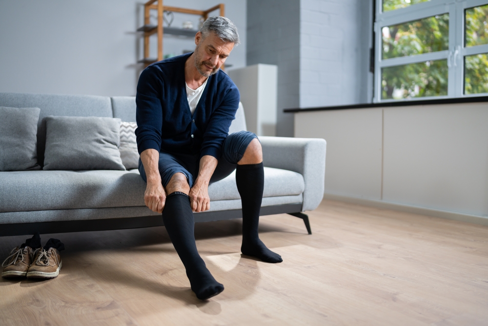Man,Putting,On,Medical,Compression,Stockings,On,Legs A man putting on compression socks.
