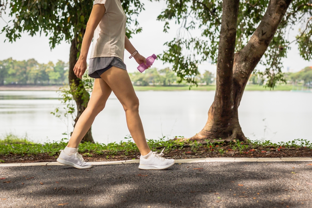 Woman,Walking,In,The,Park,With,Bottle,Water,In,Her A woman walking outside.